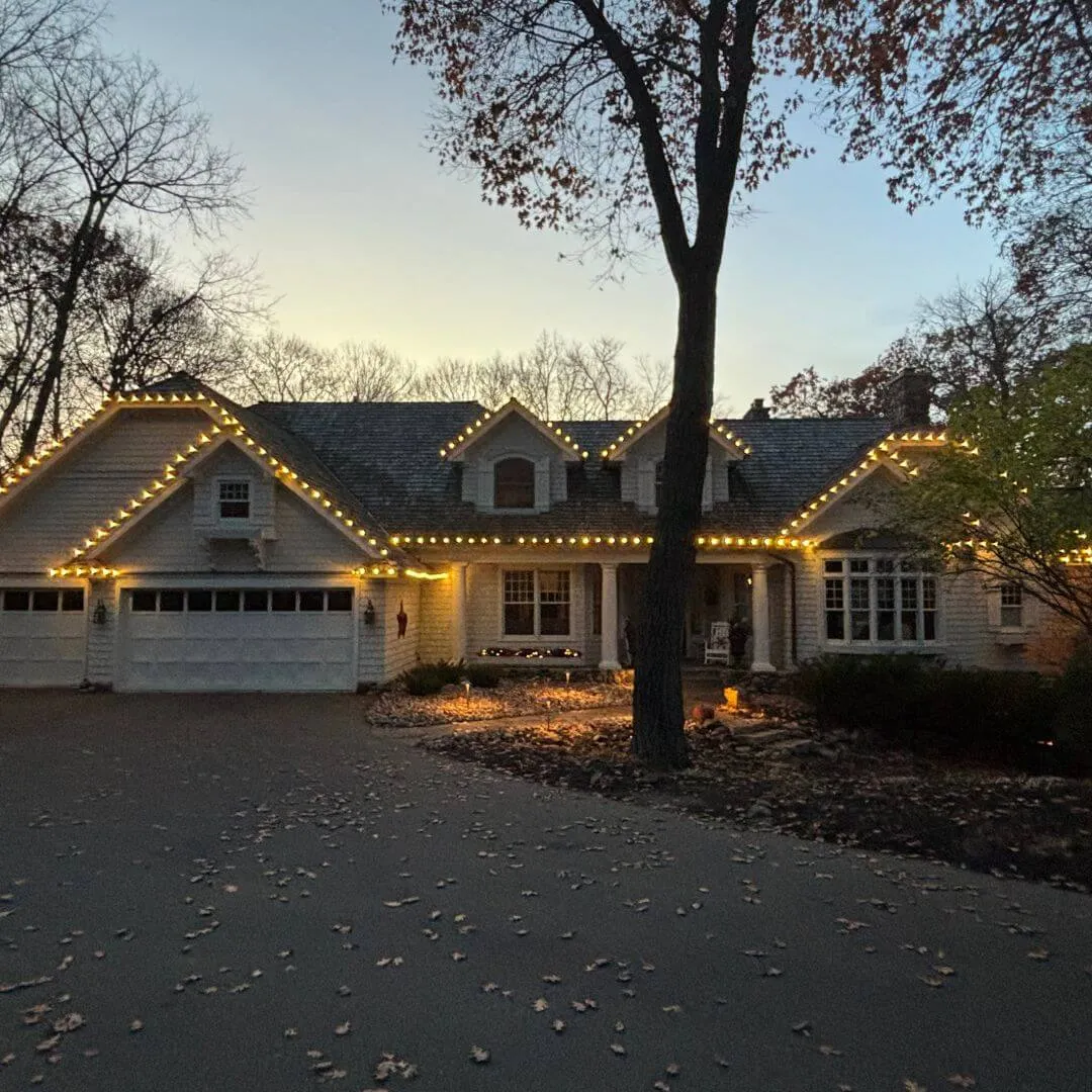 Completed Lighting Partners install: warm white roofline, gable and dormer outlining on a shingle sided ranch at dusk